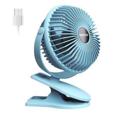 BESKAR 6-in. Clip-On Fan in light blue against a white background. A USB cable is shown next to the fan to indicate its multiple power supply options.