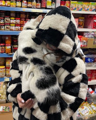 woman in checkered coat hugs black & white cat.