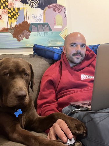 dog holds mans hand on computer mouse.