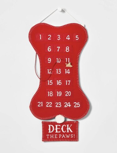 Red felt bone-shaped advent calendar for dogs with a sign underneath that reads "Deck the Paws!"
