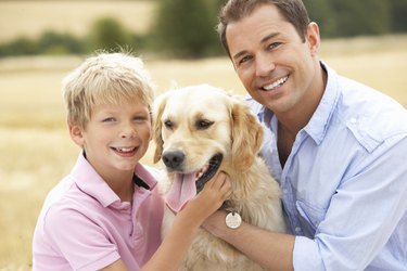 Father And Son Sitting With Dog On Straw Bales