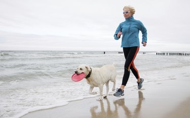 A woman jogging with her dog on the beach.