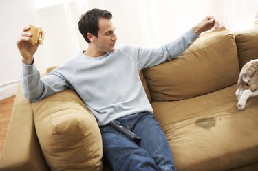 Man sitting on sofa by dog walking away from wet patch