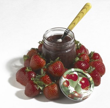 Jar of strawberry preserve nestled in fresh strawberries