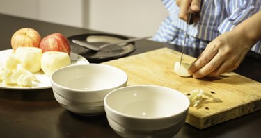 hand cutting an apple on a cutting board