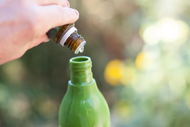 Pouring a drop of oil from a small bottle into a larger bottle outdoors