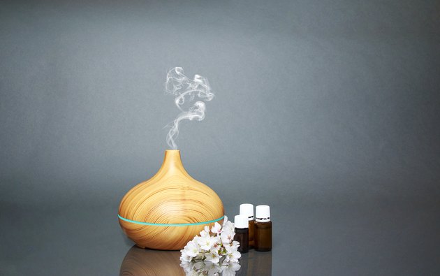 Electric Essential oils Aroma diffuser, oil bottles and flowers on gray surface with reflection.