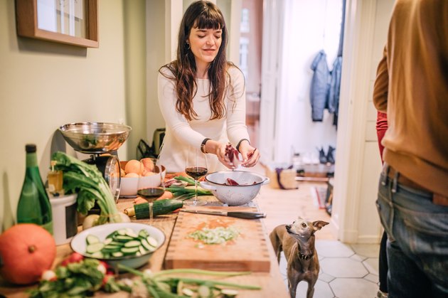 Young woman preparing meal with dog in kitchen