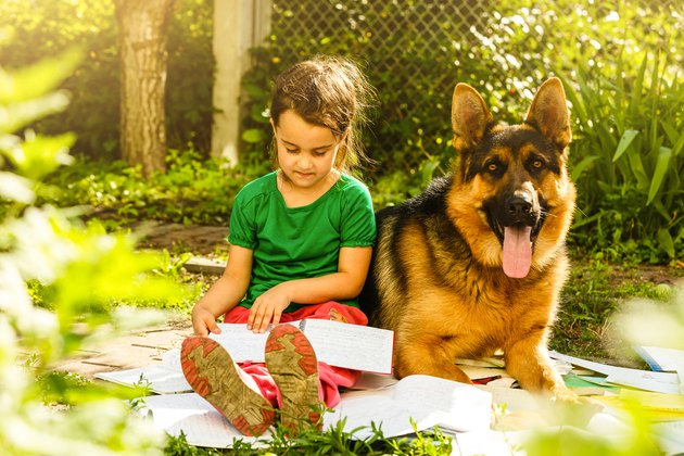 Little girl reading a book with her friend puppy dog in the outdoors.