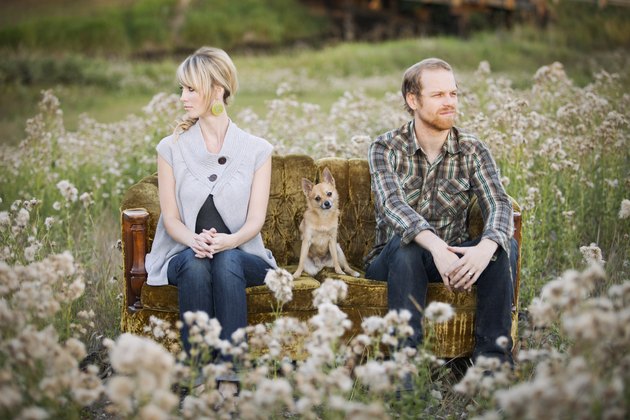 A Couple Sitting On Opposite Ends Of A Couch With A Dog In Between Them