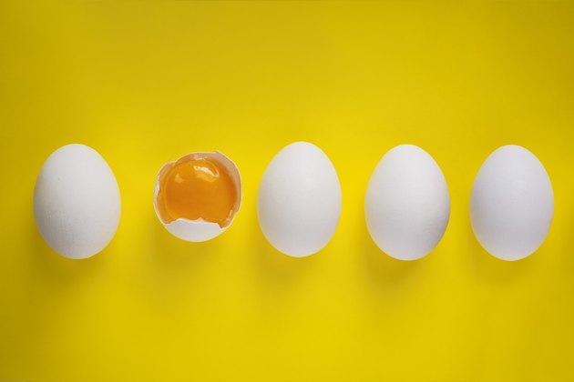 Four whole eggs and one broken egg on yellow background