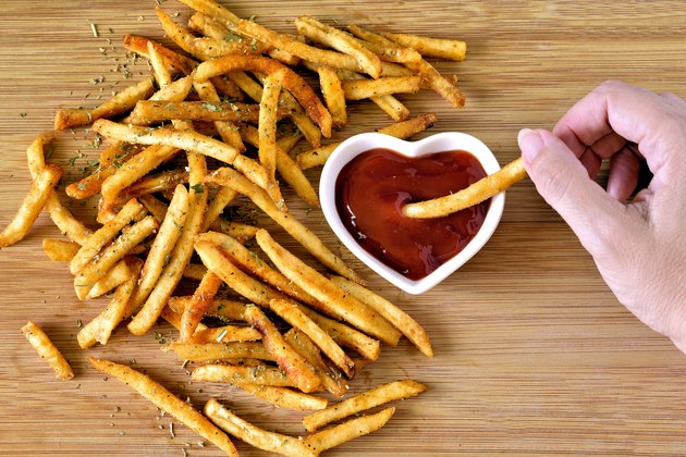French fries and ketchup, person dipping one fry in ketchup