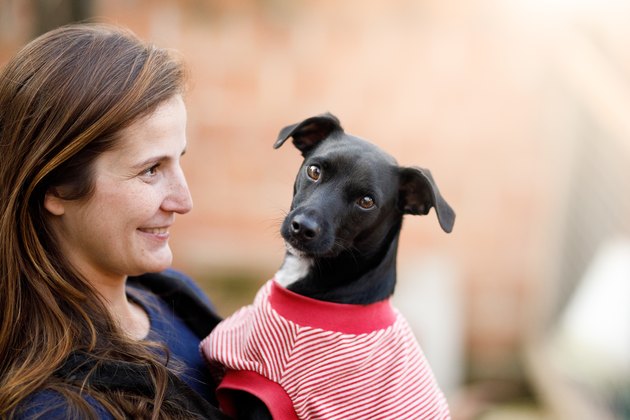 Woman holding a black dog wearing a sweater