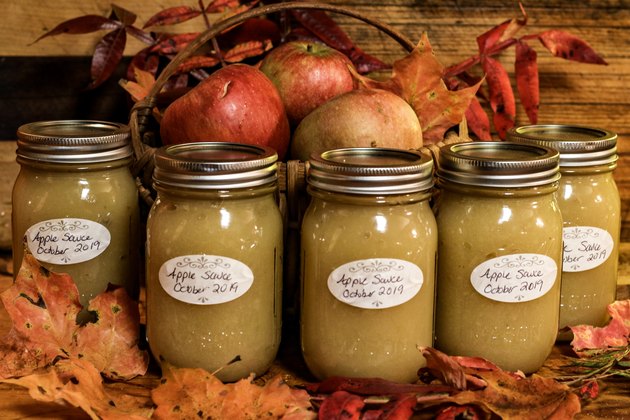 Glass jars of homemade applesauce with basket of apples and autumn leaves