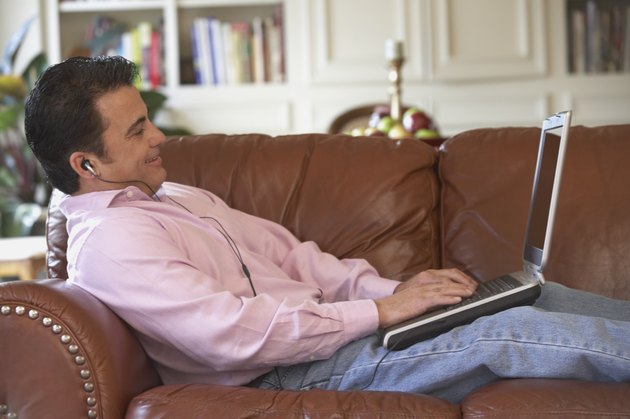 Side profile of a mid adult man lying on a couch working on a laptop