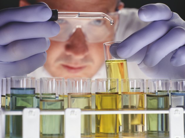 Chemist dropping liquid into test tubes, close-up