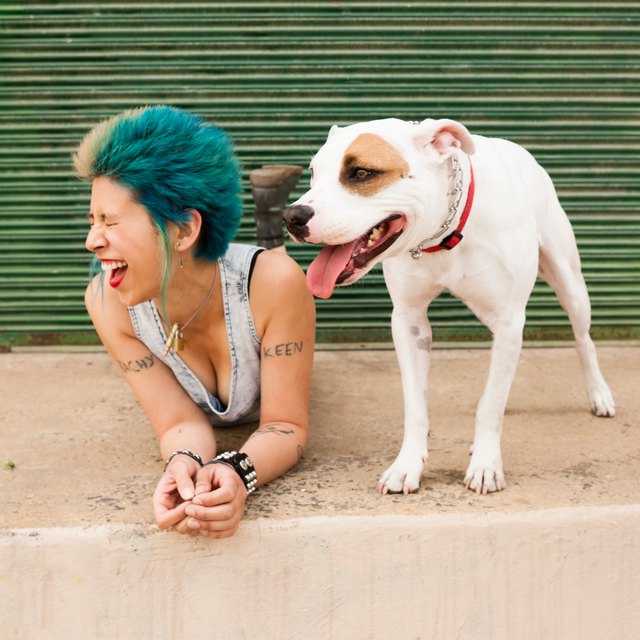 Young woman with colourful hair, lying on floor next to dog, laughing